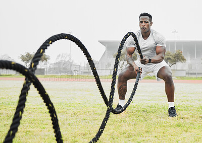 Buy stock photo Full length shot of a handsome young male athlete exercising with battle ropes outside