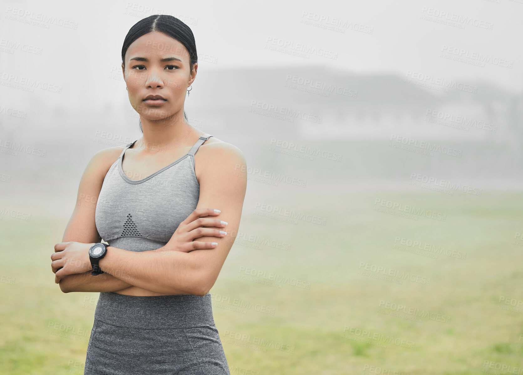 Buy stock photo Cropped portrait of an attractive young female athlete standing with her arms folded while exercising outside