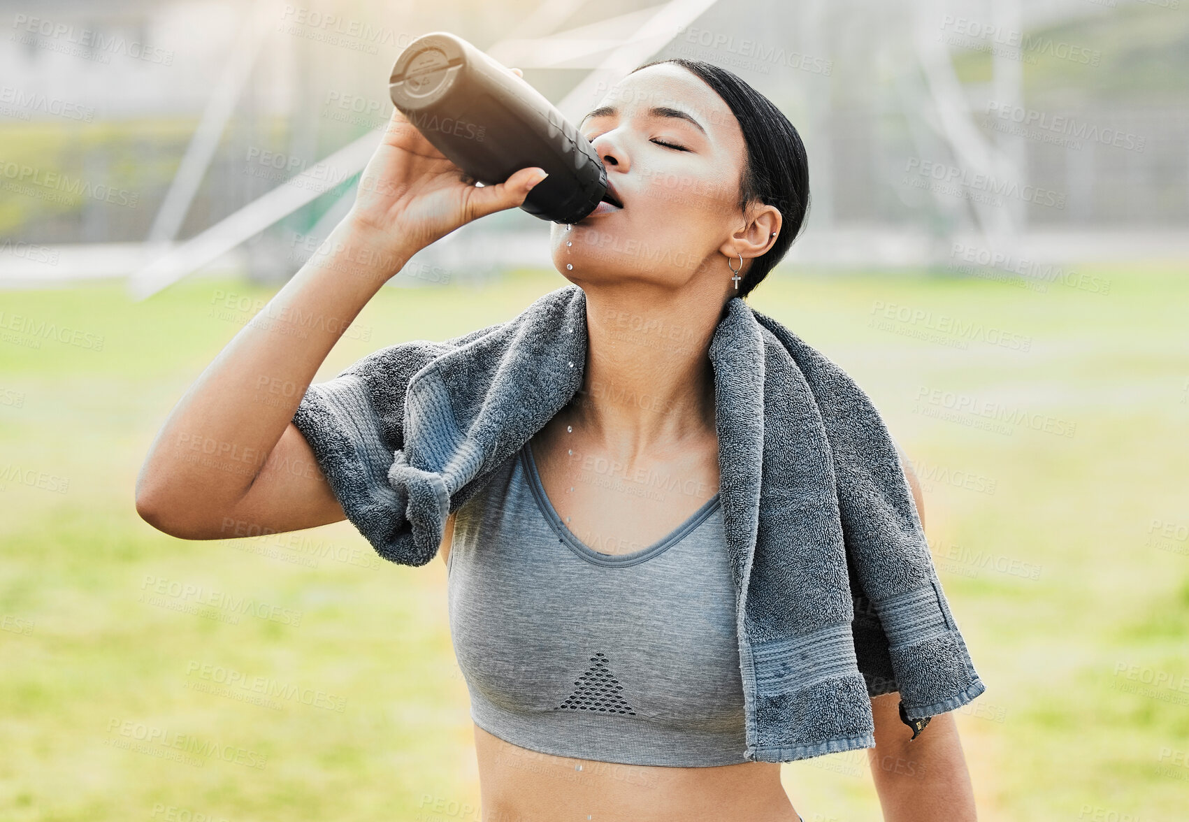 Buy stock photo Woman, thirsty and drinking water outdoor for fitness, wellness and body health goals in morning. Female athlete, bottle and hydration with liquid and towel on field for workout, training or exercise