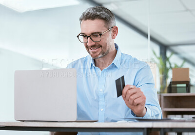 Buy stock photo Shot of a mature businessman using a laptop and credit card in an office