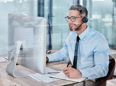 Buy stock photo Shot of a mature call centre agent writing notes while working on a computer in an office