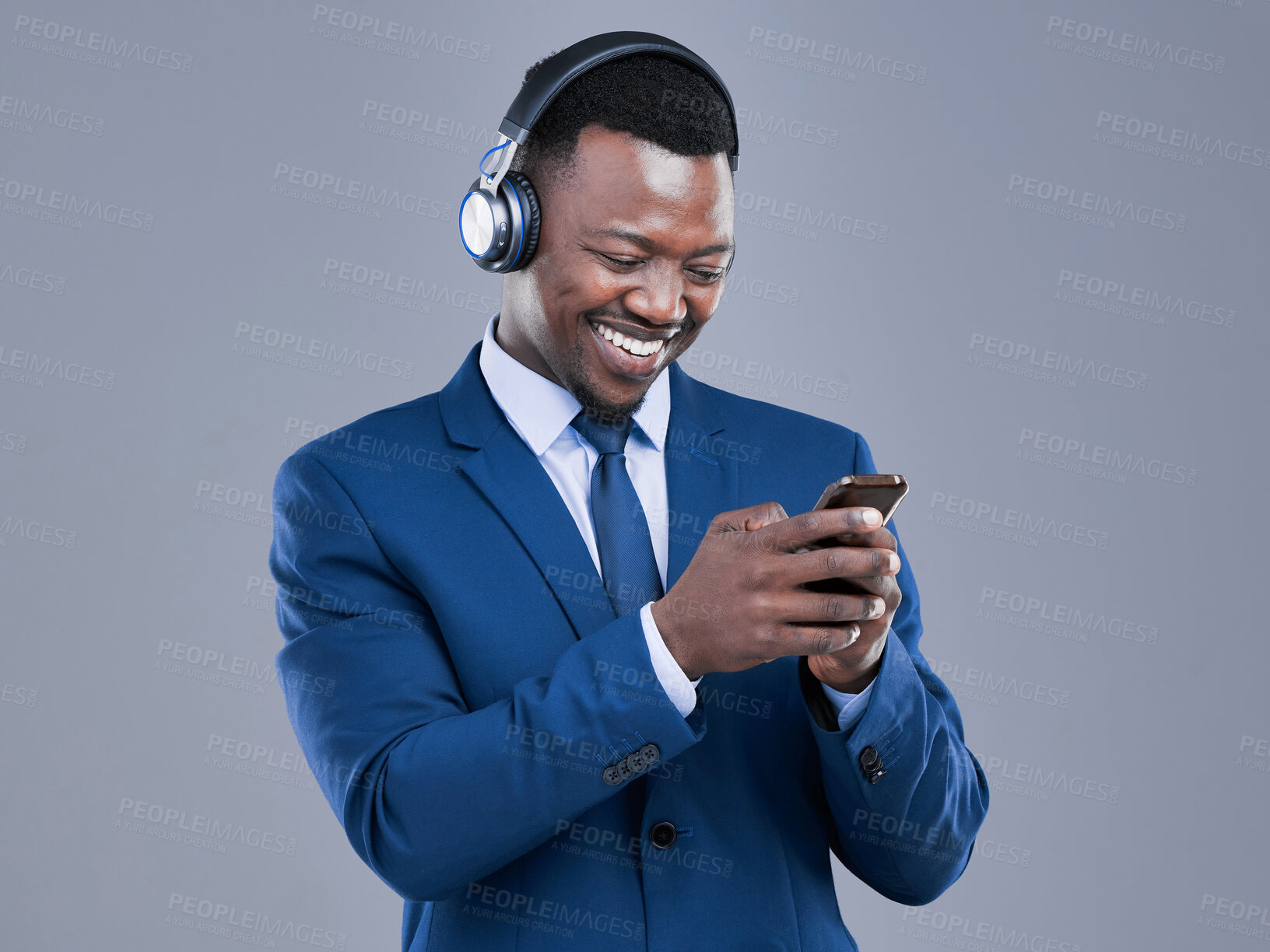 Buy stock photo Cropped shot of a handsome young businessman using his cellphone to listen to music in studio against a grey background