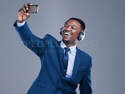 Buy stock photo Studio shot of a handsome young businessman using his cellphone to take selfies while listening to music on headphones against a grey background
