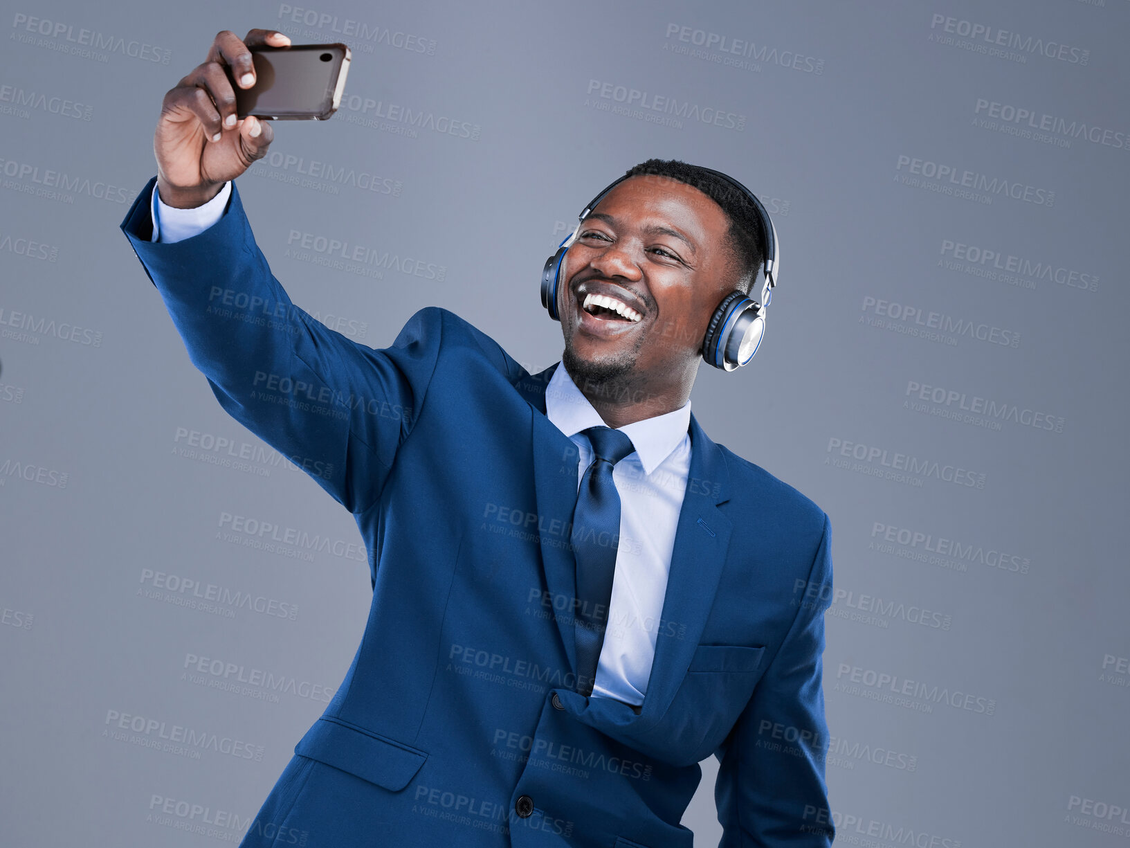 Buy stock photo Studio shot of a handsome young businessman using his cellphone to take selfies while listening to music on headphones against a grey background