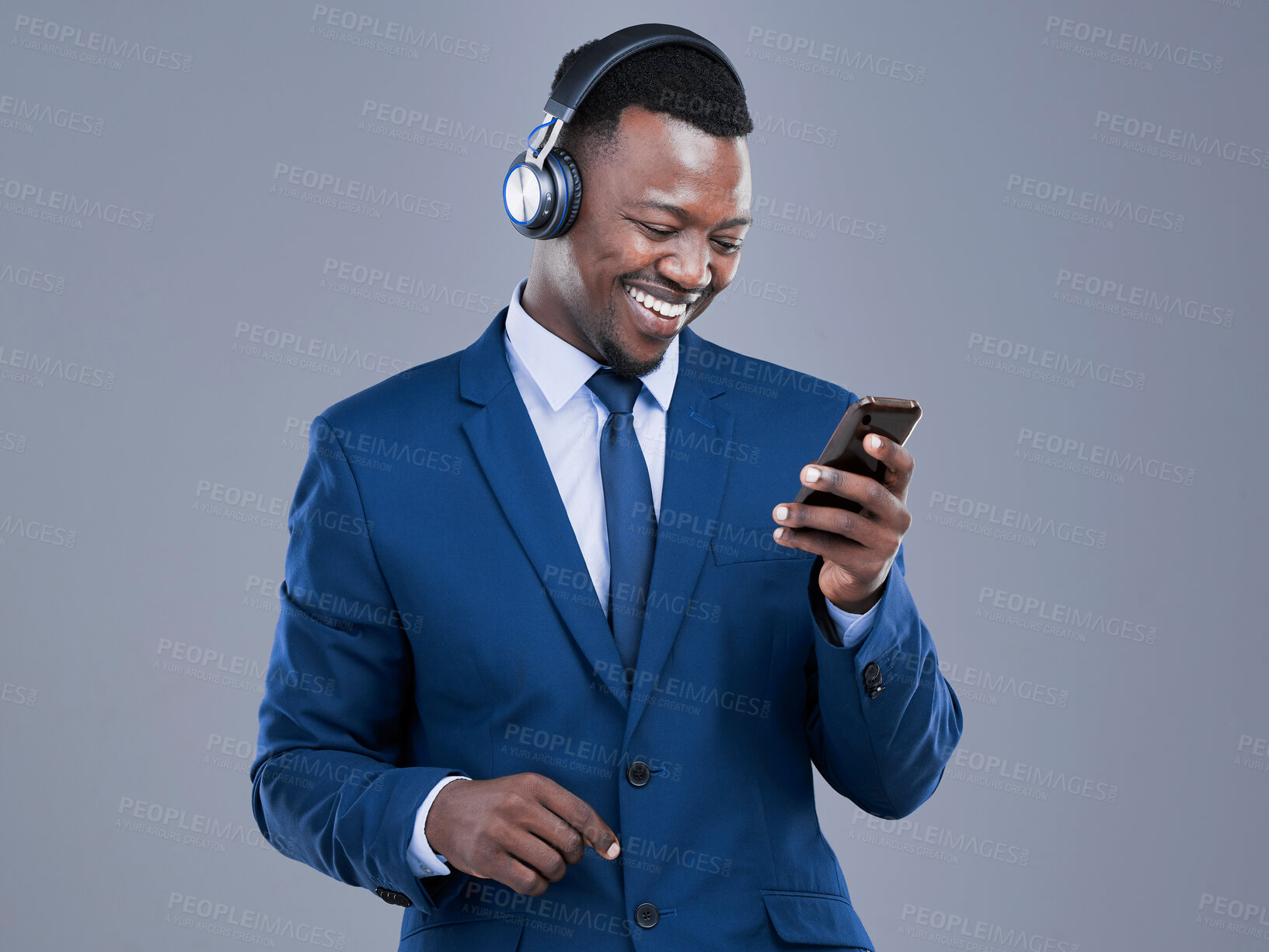 Buy stock photo Business, mobile and black man with headphones in studio for listening to music, streaming podcast or radio on gray background. Smile, lawyer and employee for social media, playlist or watching video