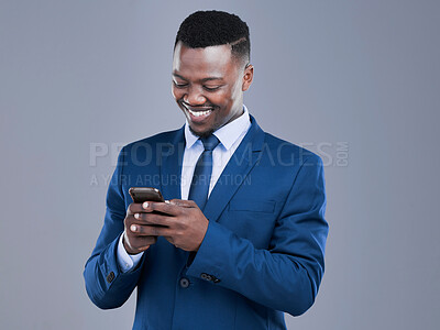 Buy stock photo Cropped shot of a handsome young businessman checking his text messages in studio against a grey background