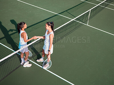 Buy stock photo Shot of two sporty young women shaking hands while playing tennis together on a court