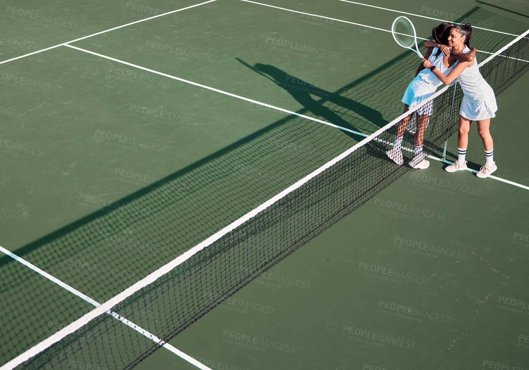 Buy stock photo Shot of two sporty young women hugging each other while playing tennis together on a court