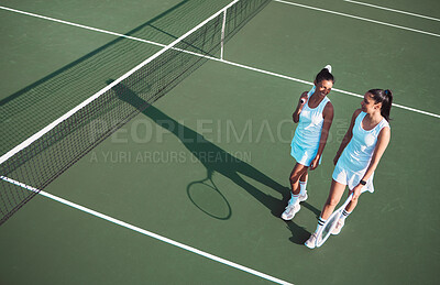 Buy stock photo Shot of two sporty young women taking a break after playing tennis on a court