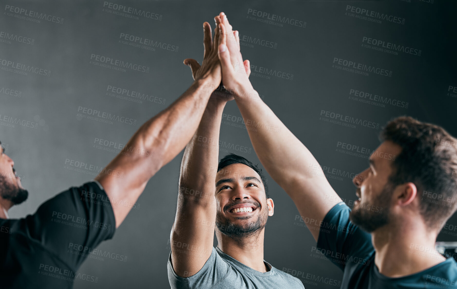 Buy stock photo Cropped shot of a group of handsome young male athletes high fiving against a grey background