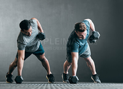 Buy stock photo Full length shot of two handsome young male athletes working out with dumbbells side by side against a grey background