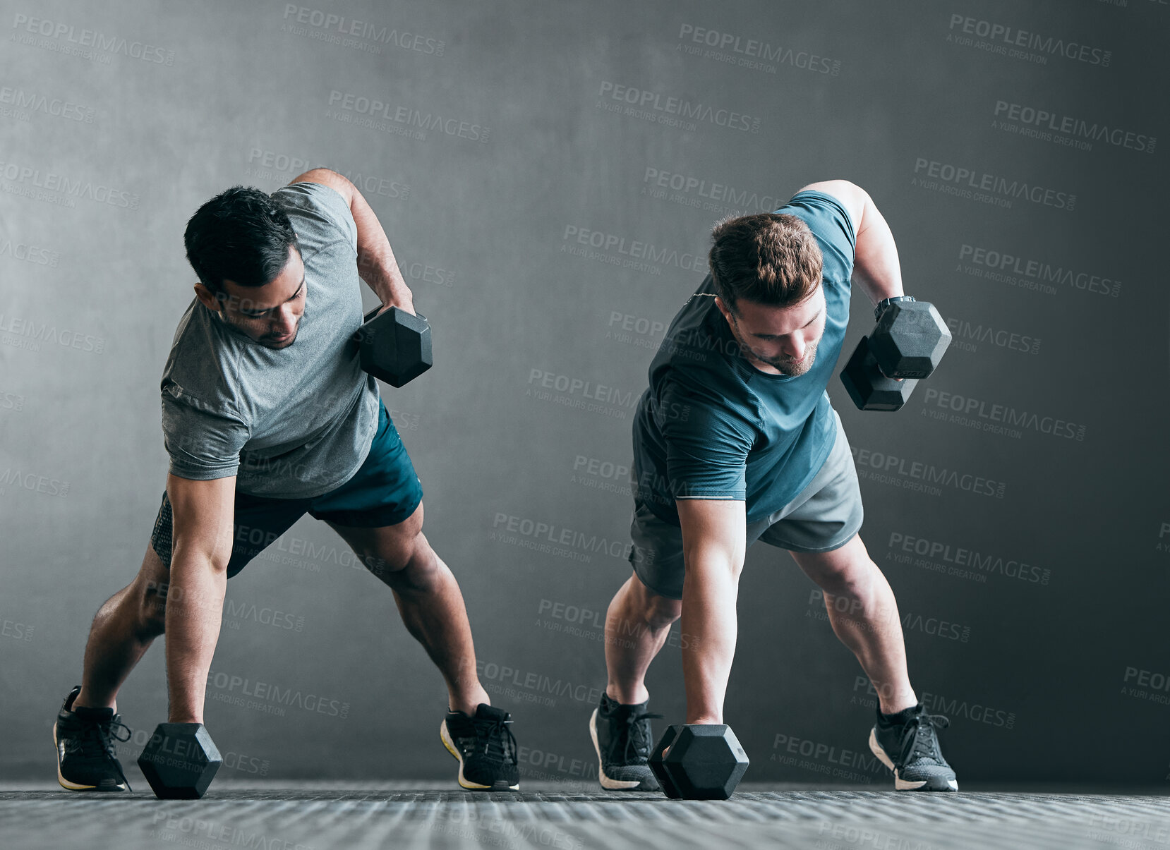 Buy stock photo Full length shot of two handsome young male athletes working out with dumbbells side by side against a grey background