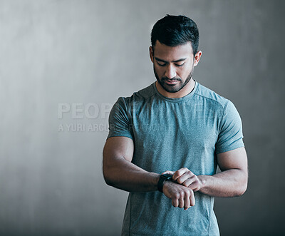 Buy stock photo Cropped shot of a handsome young male athlete checking his smartwatch against a grey background
