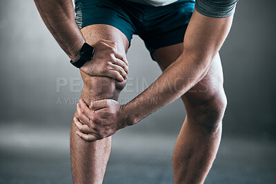 Buy stock photo Cropped shot of an unrecognizable young male athlete holding his knee in pain against a grey background