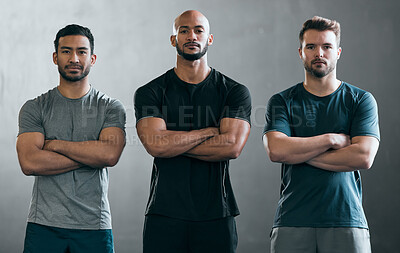 Buy stock photo Cropped portrait of three handsome young male athletes standing with their arms folded against a grey background