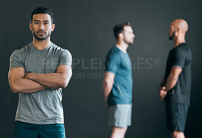 Buy stock photo Cropped portrait of a handsome young male athlete standing with his arms crossed with his friends in the distance against a grey background