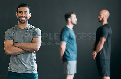 Buy stock photo Cropped portrait of a handsome young male athlete standing with his arms crossed with his friends in the distance against a grey background