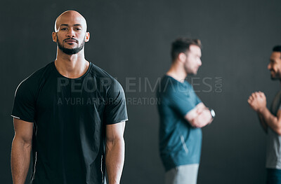 Buy stock photo Cropped portrait of a handsome young male athlete standing with his friends in the distance against a grey background