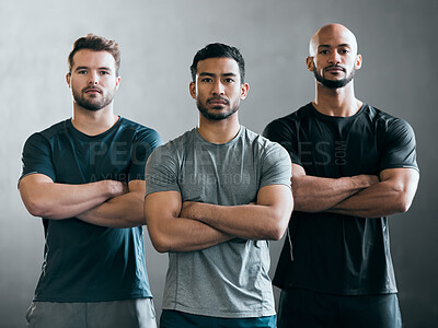 Buy stock photo Cropped portrait of three handsome young male athletes standing with their arms folded against a grey background