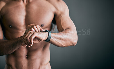 Buy stock photo Cropped shot of an unrecognizable young male athlete checking his smartwatch while standing shirtless against a grey background