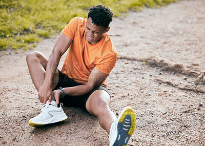 Buy stock photo Full length shot of a young man sitting alone outside and suffering from an ankle injury during his workout