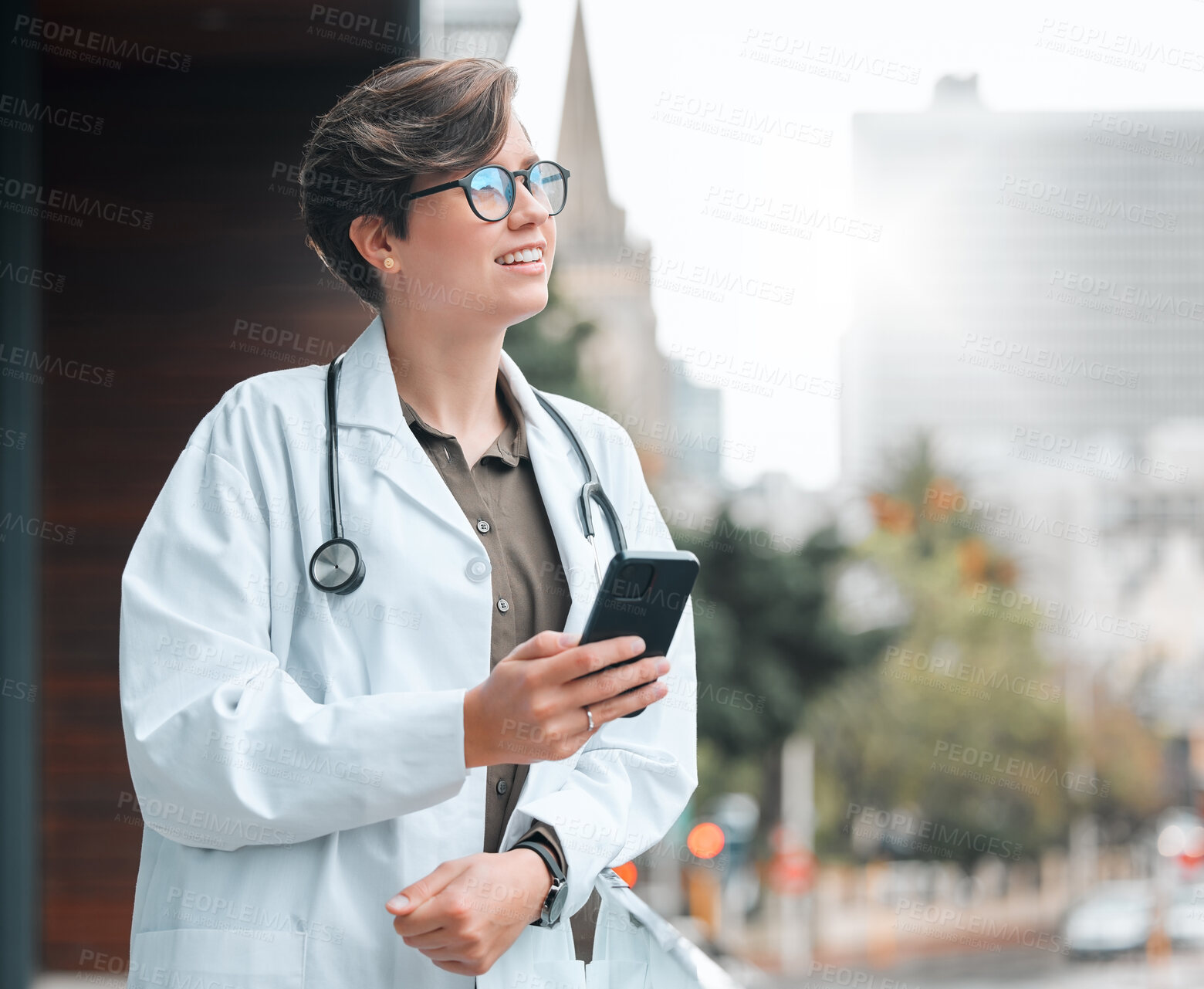 Buy stock photo Shot of a young female doctor using a phone against a city background