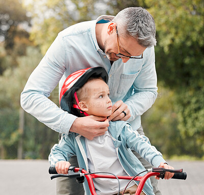 Buy stock photo Shot of a little boy sitting on his bicycle while his dad ties his helmet