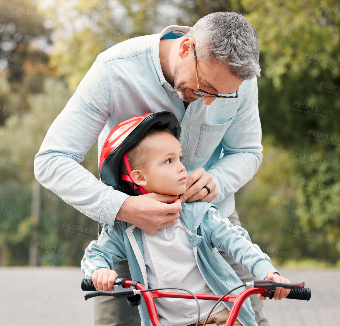 Buy stock photo Shot of a little boy sitting on his bicycle while his dad ties his helmet