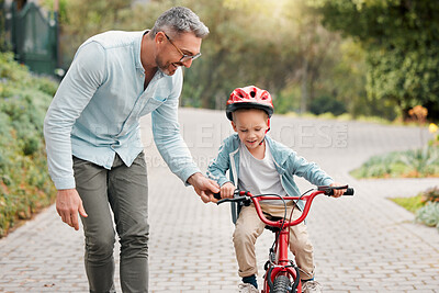 Buy stock photo Shot of a little boy wearing a helmet and riding a bike outside with his father
