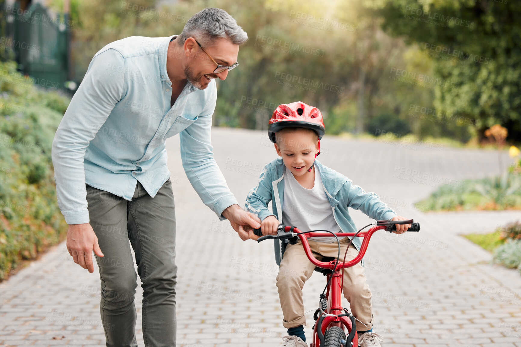 Buy stock photo Father, son and learning to ride bicycle in outdoor, parent support and training activity for kid. Dad, boy and teaching cycling outside or helping for child development, happy and helmet for safety