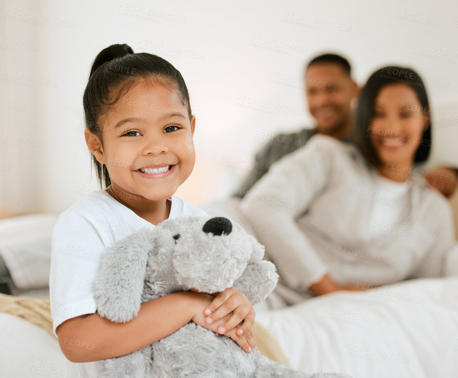 Buy stock photo Portrait of a young family settling in for bedtime while their daughter poses with a teddy in bed at home