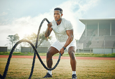 Buy stock photo Full length shot of a handsome young male athlete exercising with battle ropes outside