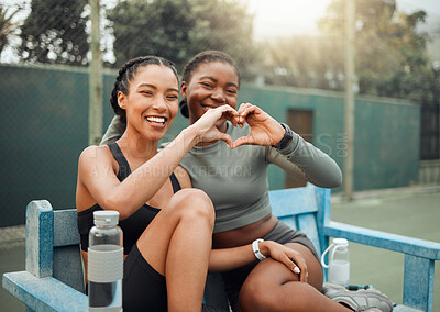Buy stock photo Cropped portrait of two attractive young female athletes making a heart shape with their hands while sitting on a bench outside during a workout