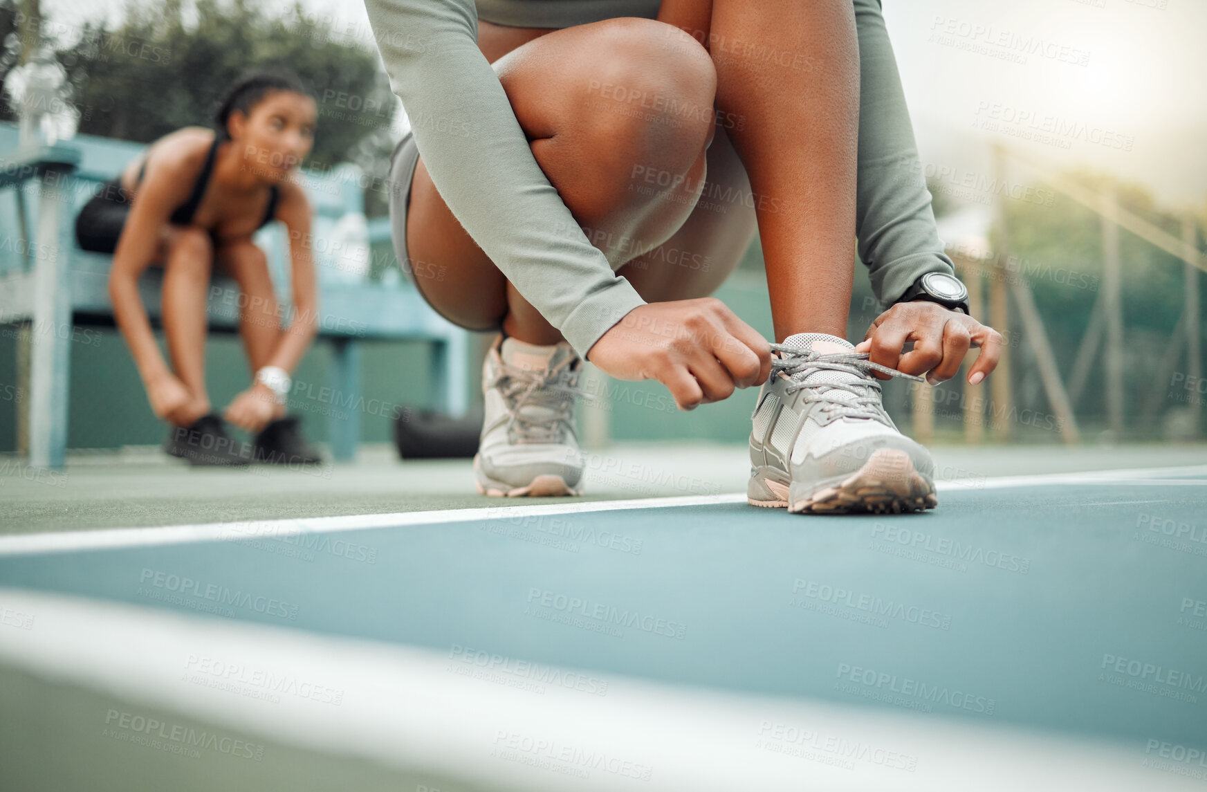 Buy stock photo Cropped shot of an unrecognizable young female athlete tying her laces during an outdoor workout with a friend in the background