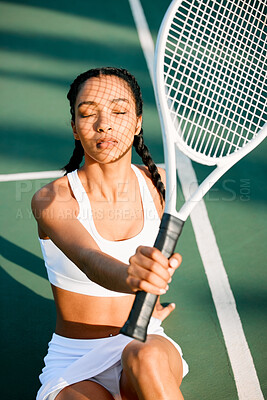 Buy stock photo Shot of a sporty young woman shielding her face from the sun with a tennis racket on a court