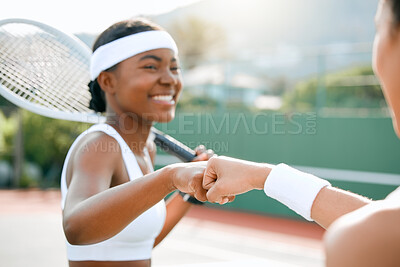 Buy stock photo Shot of two sporty young women giving each other a fist bump while playing tennis together on a court