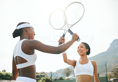 Buy stock photo Shot of two sporty young women knocking their rackets together while playing tennis on a court