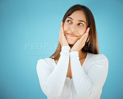 Buy stock photo Shot of a beautiful young woman holding her face and posing against a blue background
