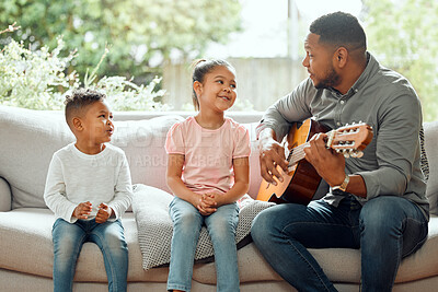 Buy stock photo Shot of a young father teaching his kids how to play the guitar while sitting on the sofa at home