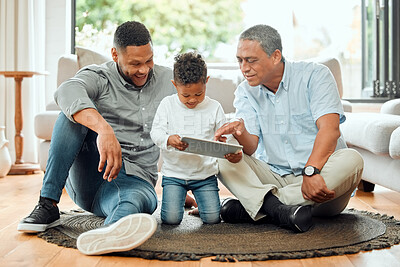 Buy stock photo Shot of an older man sitting on the floor with his son and watching his grandson use a digital tablet