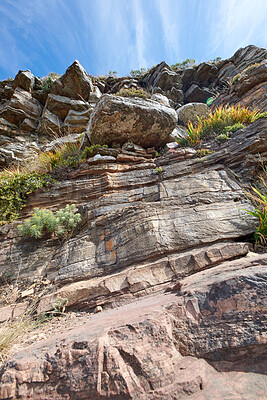 Buy stock photo Rocky mountain with big boulders for outdoor climbing while on nature adventure during summer. Landscape of lush shrubs, green plants and rocks on a cliff with blue sky in the background