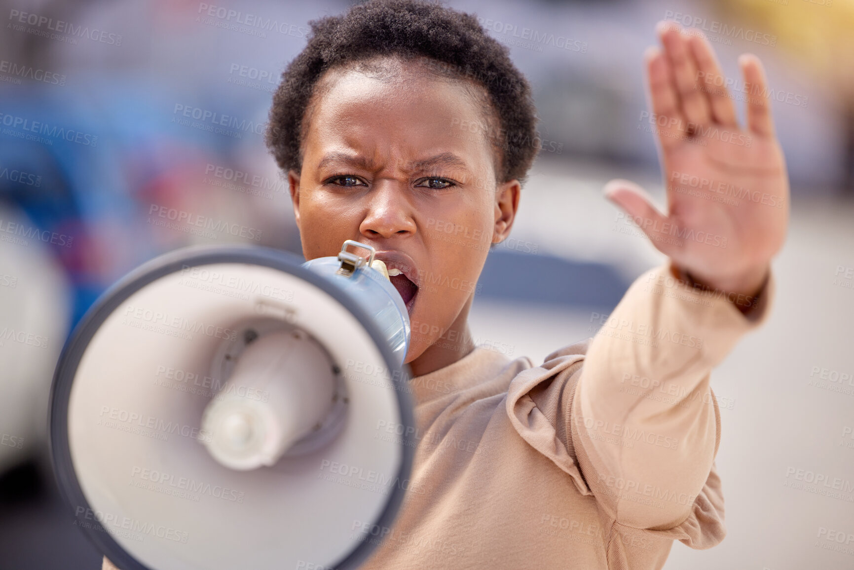 Buy stock photo Shot of a young woman with her hand raised speaking through a megaphone at a protest