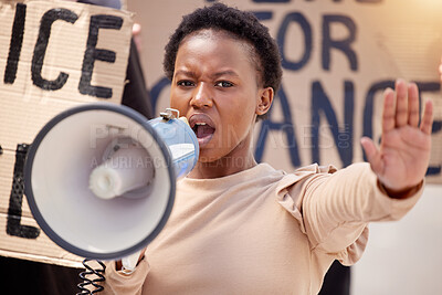 Buy stock photo Shot of a young woman with her hand raised speaking through a megaphone at a protest