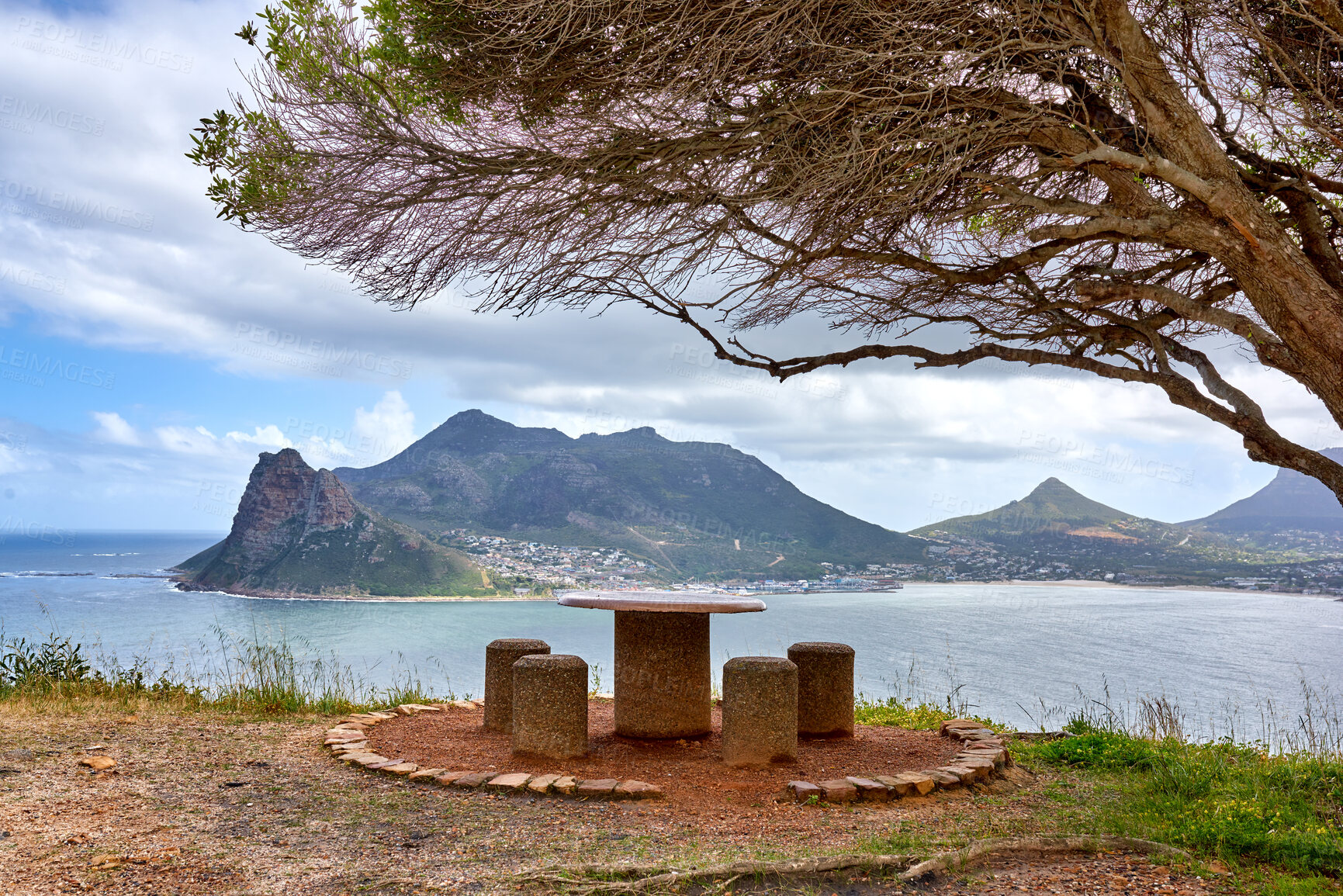 Buy stock photo Public bench overlooking the ocean and mountain looks beautiful out in nature. Landscape of four empty chairs and a table with a tree giving them shade offers a relaxing and romantic outdoor sitting