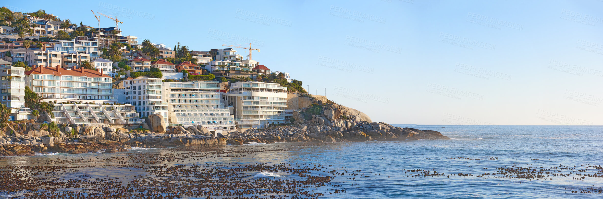 Buy stock photo Panorama of city on a mountain near the sea with a clear blue sky for copy space background. Scenic landscape of a coastal town on a hill with a quiet and calm ocean scene near Clifton, South Africa