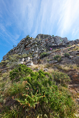 Buy stock photo Copy space on a rocky mountain with plants and shrubs growing against a cloudy blue sky background from below. Rugged and remote landscape with boulders on a cliff to explore during a scenic hike