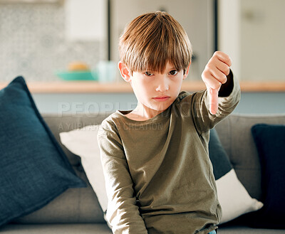 Buy stock photo Boy, home and portrait with thumbs down for disagree or opinion, no vote or review in living room. Kid, couch and hand emoji for autism feedback or protest with fail, serious in apartment with sign