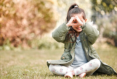 Buy stock photo Shot of a little girl forming a heart shape over her eye while sitting outside