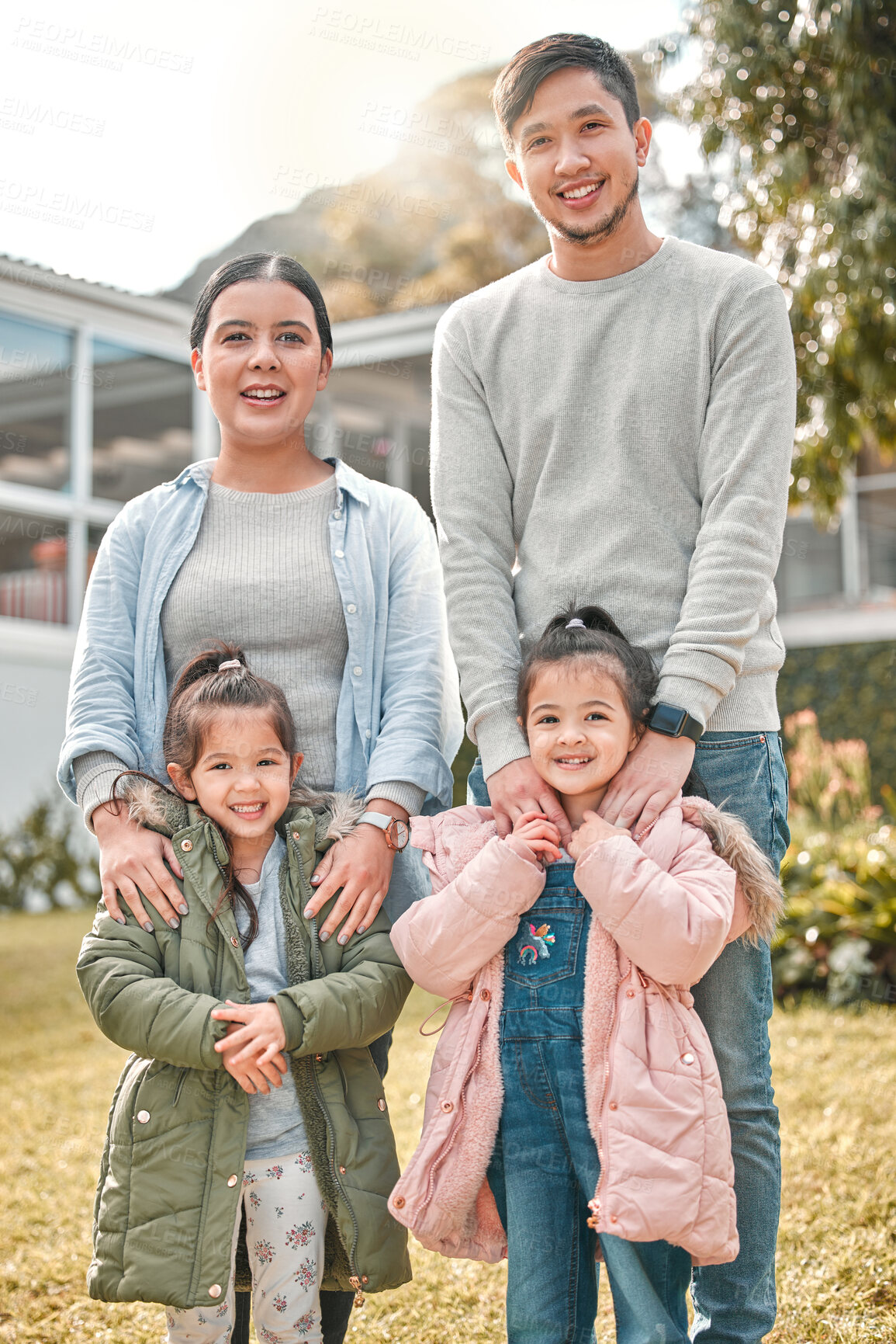 Buy stock photo Shot of a young couple and their two daughters standing outside their home
