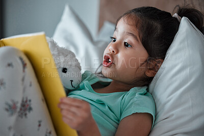 Buy stock photo Shot of a little girl reading a book while lying on her bed